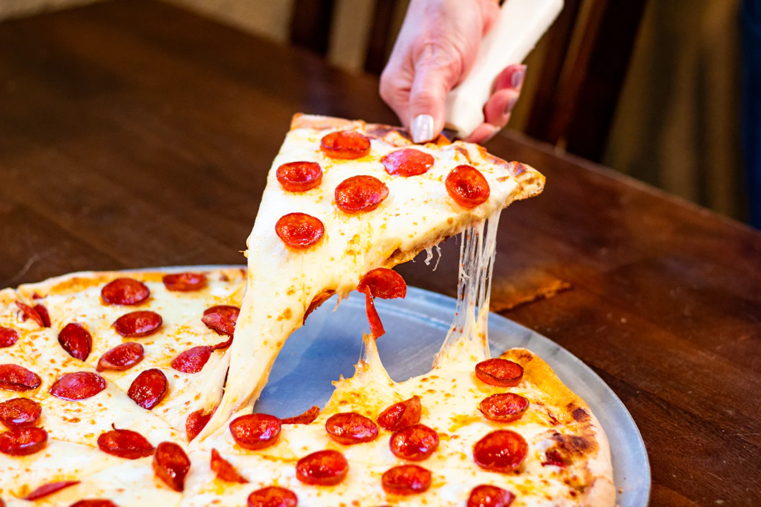 A cheesy slice of pepperoni pizza being lifted