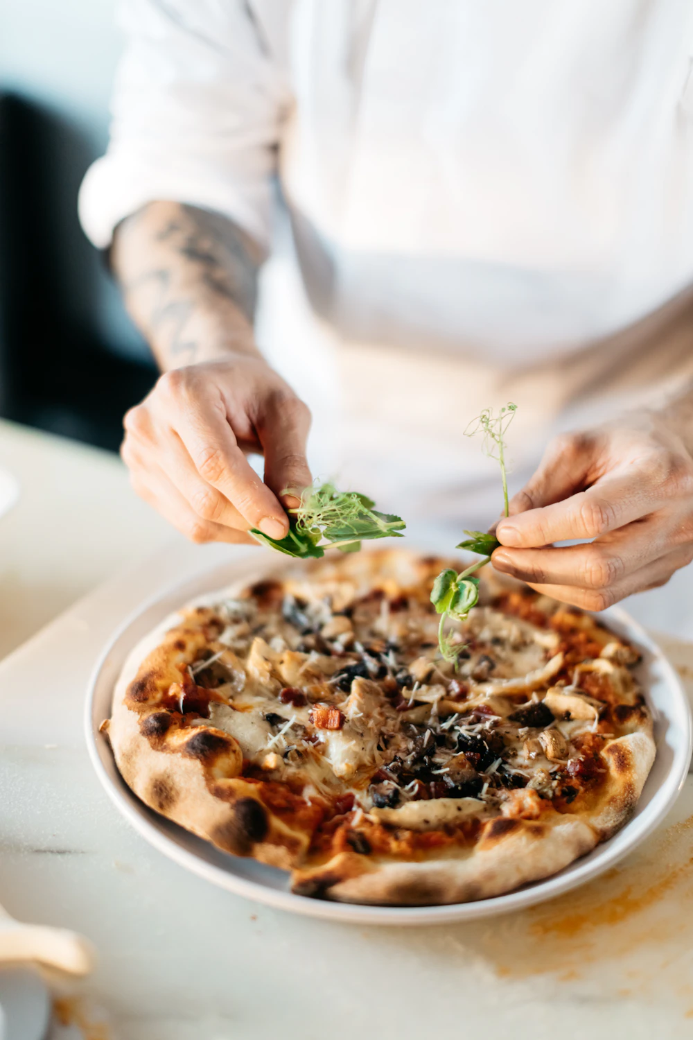 A pizza maker adding toppings to a pizza